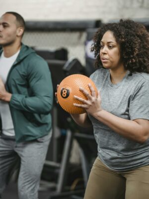 Concentrated young diverse trainer and athlete exercising with medicine balls in gym