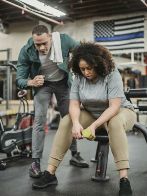 Trainer helping plump woman exercising with dumbbell